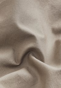 Beżowa tkanina tekstylna o gładkiej strukturze, z delikatnym splotem tworzącym subtelne wzory i miękkie układanie.