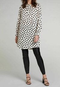 Tunica a pois in crema con pois neri, caratterizzata da un collo rotondo e maniche lunghe. Abbinata a leggings in pelle nera e tacchi a strappo.