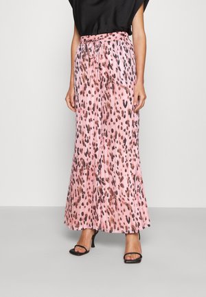 Mujer con pantalones anchos plisados rosa con estampado de leopardo marrón y negro, top negro y sandalias negras de tacón.