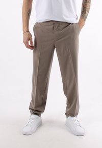 Pantaloni beige su misura con una texture morbida, dotati di tasche laterali e una vestibilità comoda, abbinati a sneakers bianche.