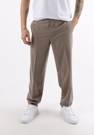 Pantaloni beige su misura con una texture morbida, dotati di tasche laterali e una vestibilità comoda, abbinati a sneakers bianche.