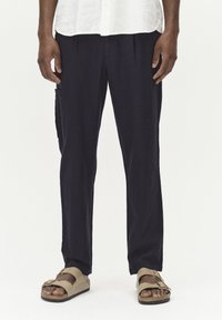 Kraljevsko plave lanene hlače s opuštenim krojem, koje imaju bočni cargo džep i su uparene s bež sandalama. Tkanina ima mekanu teksturu.