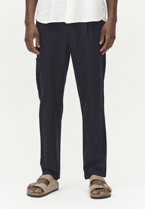 Pantaloni din in navy, cu o croială lejeră, având un buzunar cargo pe lateral și asortați cu sandale bej. Materialul are o textură moale.