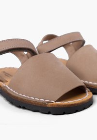 Sandali in suede marrone con design a punta aperta. Presentano due cinghie incrociate e un accento bianco cucito lungo la suola. Suola in gomma.