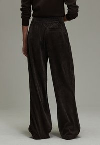 Szerokie spodnie sztruksowe w ciemnym brązie. Teksturowany materiał z pionowymi prążkami, elastyczny pas i pojedyncza kieszeń z tyłu.