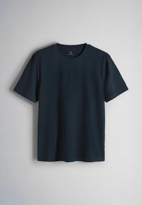 T-shirt semplice blu scuro a maniche corte con scollo rotondo appesa su uno sfondo grigio chiaro.