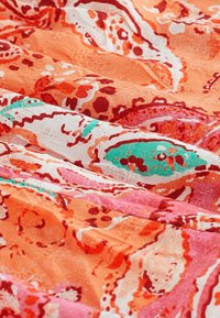 Tissu à motifs orange et rose avec des accents verts, présentant une texture fluide et des dessins abstraits complexes partout.