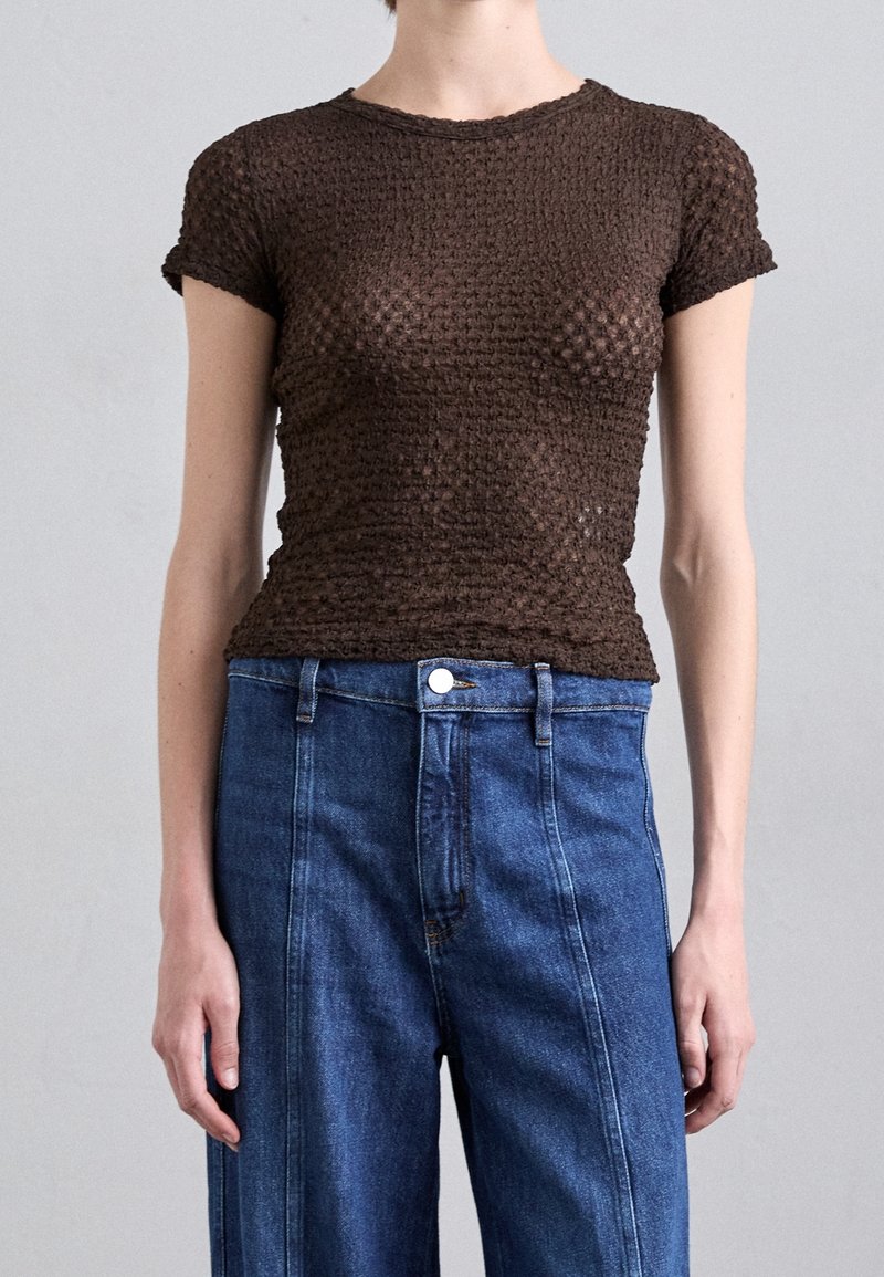 Braun strukturiertes Strickoberteil mit kurzen Ärmeln, taillierter Passform, kombiniert mit hochgeschnittenen blauen Jeans aus Denim, die einen Knopfverschluss und seitliche Taschen haben.