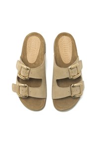 Sandali in suede beige con due cinturini regolabili e fibbie dorate. Suola piatta con un dettaglio a insole testurizzata.