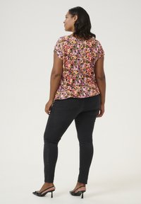 Haut à manches courtes floral en rose, jaune et vert sur un fond noir ; associé à un jean skinny noir et des sandales à talons noires.