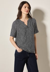Blusa a maniche corte nera e bianca con motivo, design a V e tessuto testurizzato, indossata con pantaloni in denim blu scuro.