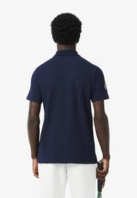 Polo de manga corta en azul marino con textura acanalada, que presenta un cuello clásico y un detalle de logotipo bordado en el hombro izquierdo.