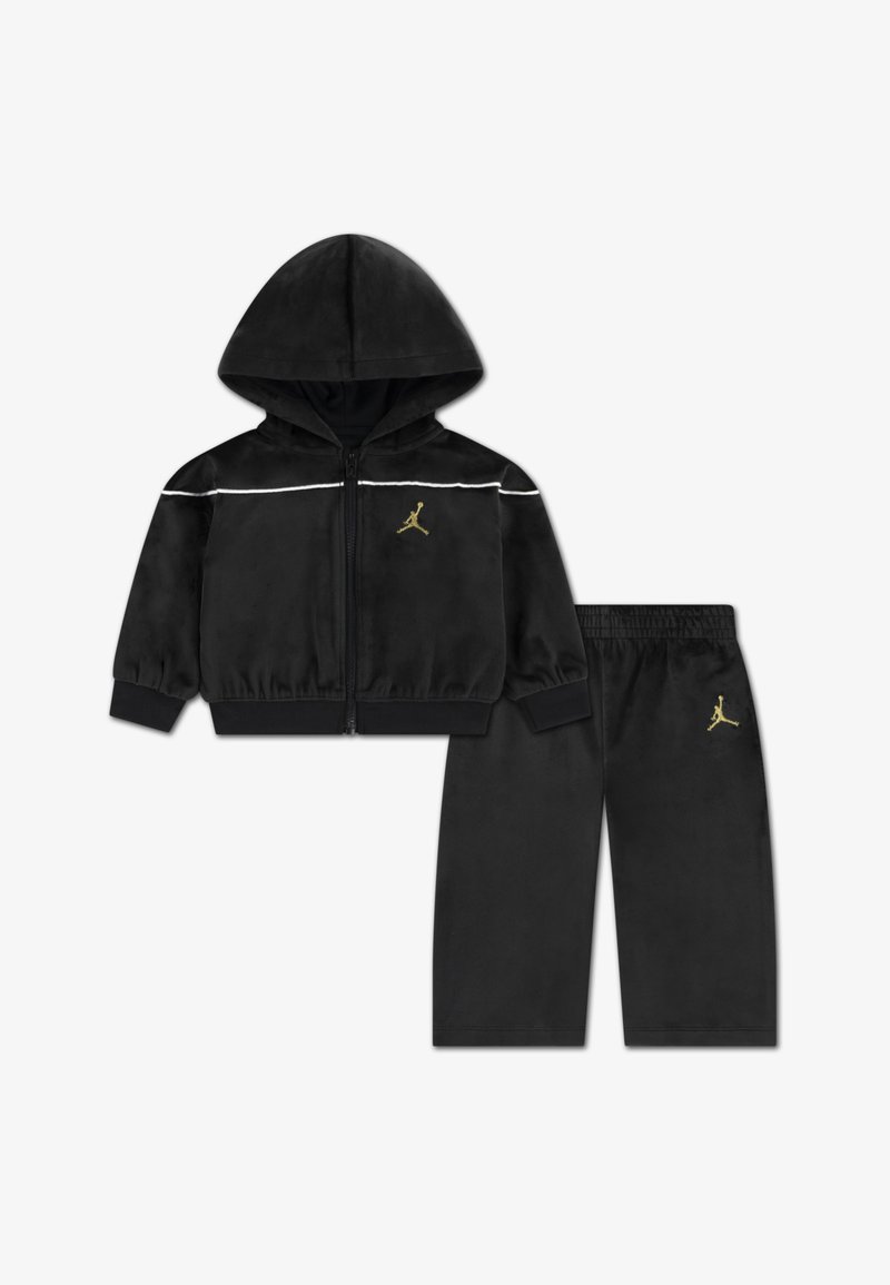Sort velour træningsdragt med en lynlås-hoodie og matchende bukser. Har hvide striber og et gyldent logo på begge dele.