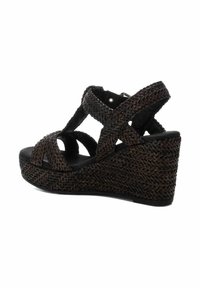 Sandalía de cuña trenzada en marrón con correas entrelazadas, suela negra y superficie texturizada. Cuenta con correa para el tobillo y un tacón de aproximadamente 3 pulgadas.