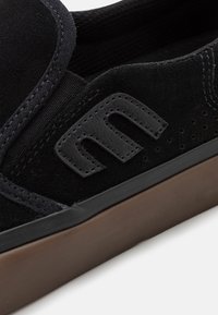 Černá semišová nazouvací bota s gumovou podešví. Má prošití a texturovaný detail na boku. Minimalistický design.