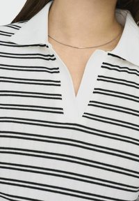 Stribet top i sort og hvid med kravehalsudskæring, der har en V-formet åbning. Glat strikket stof med jævn tekstur og kontrasterende striber.