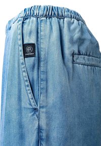 Világoskék farmernadrág elasztikus derékrésszel, oldalzsebekkel és hátsó zsebekkel, valamint fekete téglalap alakú márkajelzéssel az oldalzseb mellett.