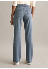 Lichtblauwe rechte jeans met hoge taille, voorzien van twee achterzakken en lichte vervaging, gecombineerd met witte sneakers.