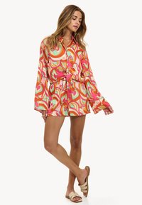 Camisa corta y colorida de botones con un diseño audaz y ondulante en rosa, naranja y verde. Mangas largas con cintura ajustada y cuello plano.