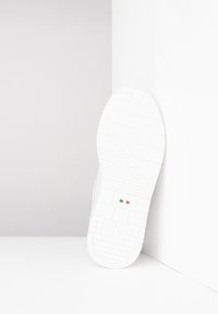 Semelle de basket blanche avec un caoutchouc texturé et des motifs géométriques, marquée d'un petit détail du drapeau italien. Design épuré et moderne.