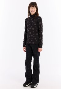 Haut noir à manches longues avec un motif d'étoiles grises, col zippé, associé à un pantalon noir présentant un design d'étoiles similaire, porté avec des bottes noires.