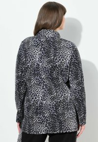 Chemise à manches longues en tissu doux avec un motif léopard gris et noir. Comprend un col montant et un ourlet légèrement arrondi.