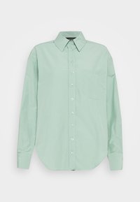 Camicia a maniche lunghe verde chiaro con colletto a punta e una tasca sul petto, esposta su uno sfondo bianco semplice.