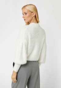 White, fluffy sweater with loose sleeves and a round neckline, paired with gray tailored pants. Focus on soft texture and relaxed fit.