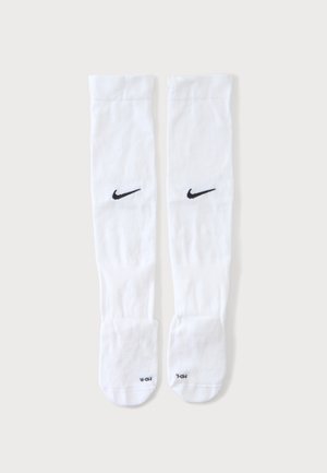 Pár bielych Nike podkolienok s čiernymi logami swoosh a veľkostnými štítkami na častiach chodidiel, zobrazený na jednoduchom pozadí.