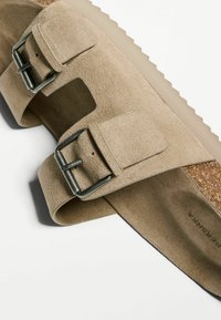 Beige velúr szandál két állítható pánttal, texturált felülettel és fémbuckle-okkal. Paraffin talpbetét és bordázott gumitalp a stabilitás érdekében.