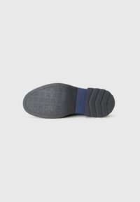 Black rubber shoe sole with textured grip pattern and a blue accent section. Chunky heel design with a slight curve at the toe.