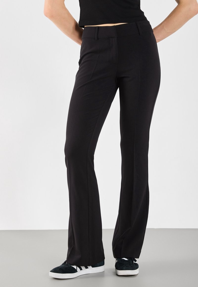 Black tailored pants with a slim fit, featuring a flat front, subtle pleats, and a smooth, stretchy fabric for comfort.