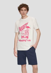 Camiseta blanca de algodón con un diseño gráfico en rosa de una bebida con hielo, limón y un flamenco. Combinada con pantalones cortos azul marino.