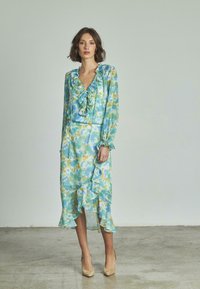 Langärmliges Kleid in blauem und grünem Batikmuster mit Rüschen entlang des Ausschnitts und Saums, mit Knopfdetails und fließender Silhouette.