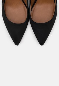 Schwarze Wildleder-Pumps mit spitzem Zehenbereich und glattem braunem Innenleben. Minimalistisches Design mit schlanker Silhouette und ohne sichtbare Hardware oder Akzente.