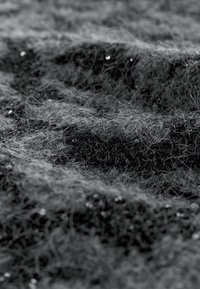 Strukturirani materijal u nijansama crne i sive, s neravnomjernim valovima i finim, pahuljastim vlaknima s malim reflektirajućim detaljima raspoređenim posvuda.