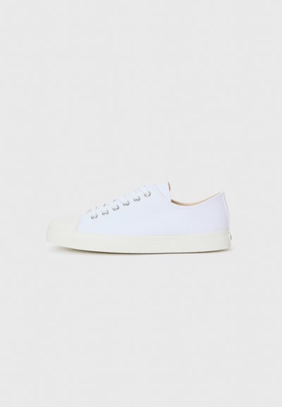 Sneaker bianca in tela con punta arrotondata, gomma nella parte anteriore e suola piatta. Presenta occhielli metallici e un semplice design con lacci.