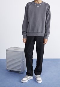 Sudadera gris con cuello redondo, puños y dobladillo de canalé, combinada con pantalones negros de corte holgado y zapatillas gris y blancas. Accesorios en tono plateado.