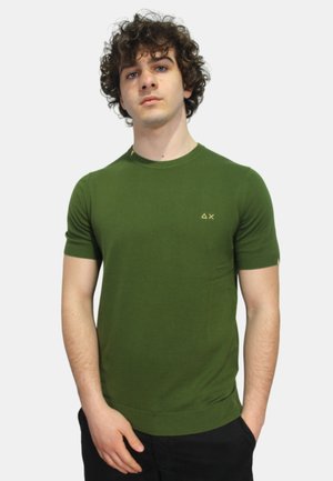 T-shirt verde a manica corta realizzato in un tessuto liscio. Presenta un collo rotondo e un piccolo logo dorato sul lato sinistro. Design semplice e aderente.