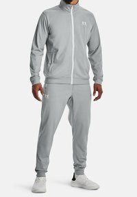 Grå atletisk träningsdress i slät tyg med en zip-up jacka med hög krage och matchande byxor. Logotyp på bröst och lår.