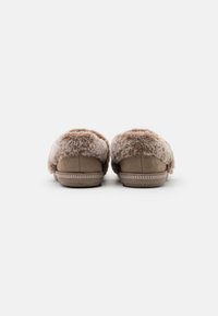 Bruine suède slippers met een pluizige bontrand, met een afgeronde vorm en een subtiele stikselafwerking aan de basis. Zachte textuur overal.