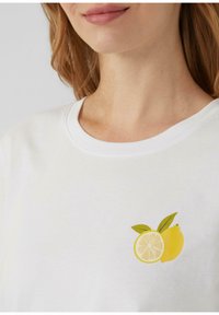 T-shirt blanc avec un petit graphique d'un citron et une tranche de citron avec des feuilles vertes, encolure ronde et texture de tissu douce.