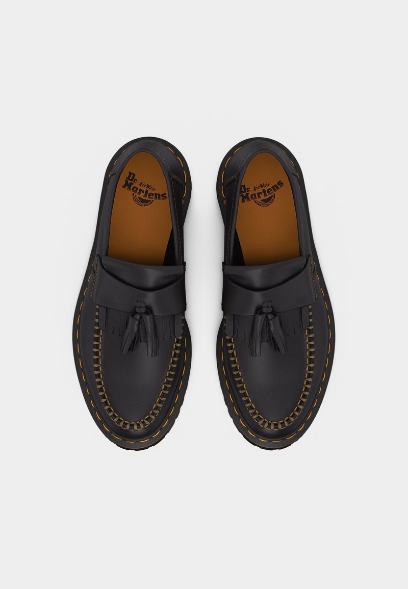 Pair of black leather Dr. Martens loafers featuring fringe and tassel details, yellow stitching, and branded insoles, viewed from above.