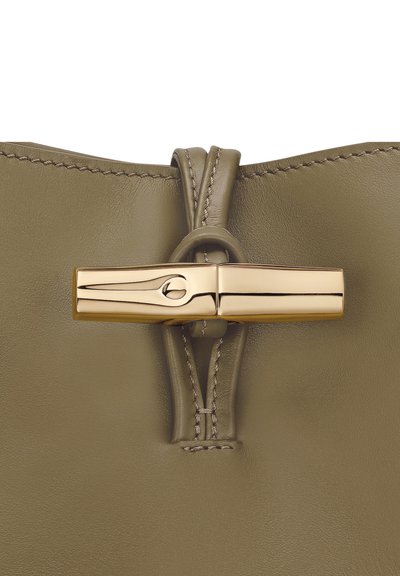 Olive green leather bag closure featuring a gold-tone clasp with a streamlined design and visible stitching along the edges.