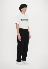 White t-shirt with "No Problem" printed in black, paired with loose-fitting black trousers and white sneakers. Simple design, casual style.