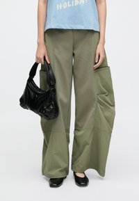 Χακί παντελόνι φαρδύ με μεγάλες πλαϊνές τσέπες, συνδυασμένο με ανοιχτό γαλάζιο t-shirt. Μαύρη τσάντα με υφή, μαύρα επίπεδα παπούτσια, λιτές λεπτομέρειες.