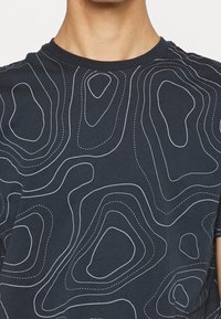 Námořnické tričko s kulatým výstřihem, které má bílý vlnitý konturový vzor. Vyrobeno z bavlny s jemnou, hladkou texturou.