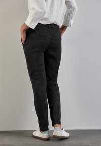 Svarta byxor med en slät yta och elastisk midja, med två bakfickor. Matchas med vita sneakers.