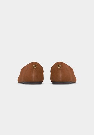 Paire de chaussures en daim marron à enfiler, vues de dos, avec de petits détails ronds en métal doré près du talon sur fond blanc.