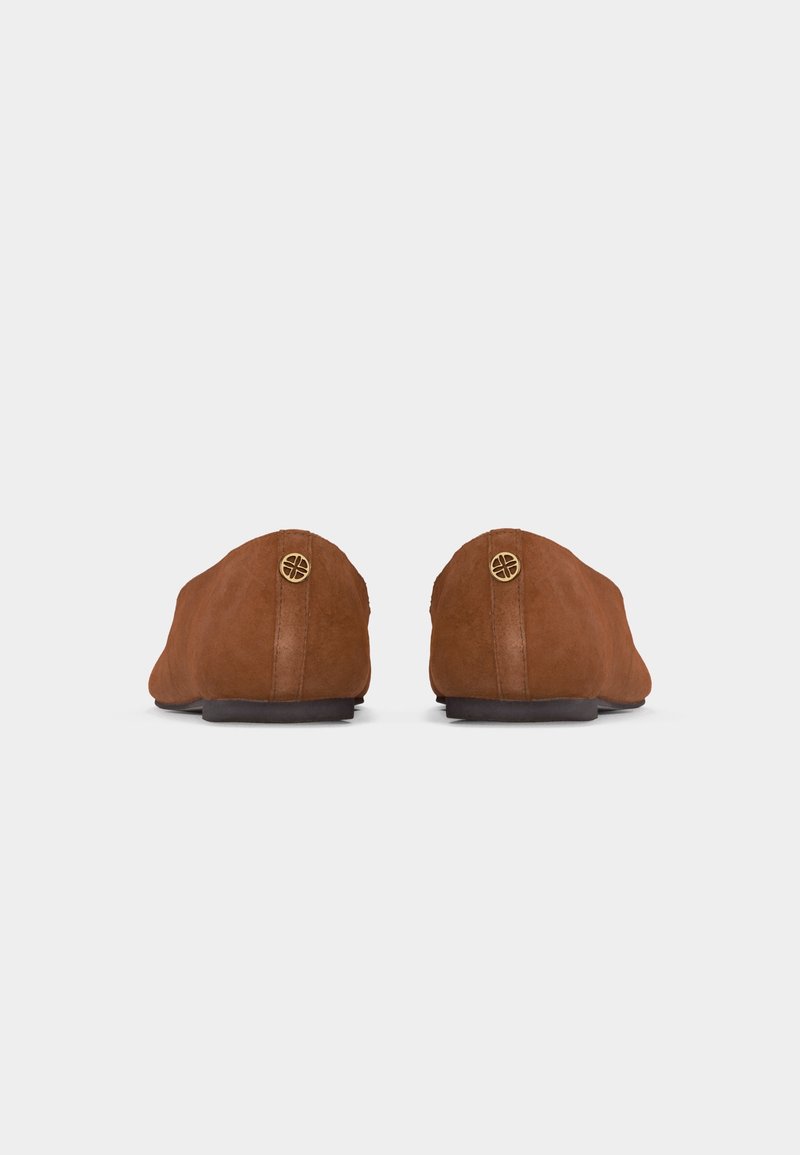Paire de chaussures en daim marron à enfiler, vues de dos, avec de petits détails ronds en métal doré près du talon sur fond blanc.